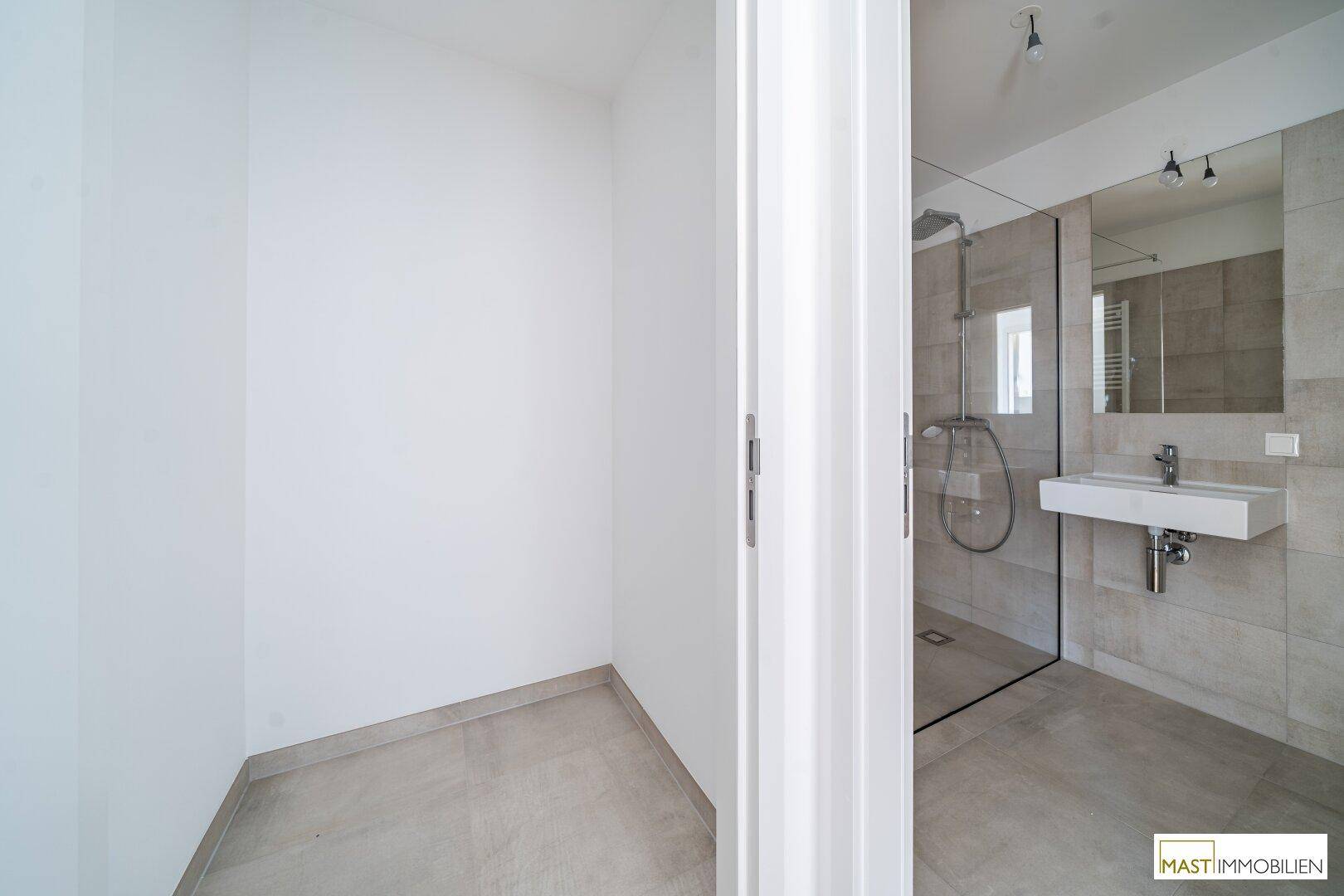 Geräumiges Badezimmer mit moderner Dusche und neutralen Fliesen, bietet viel Platz.
