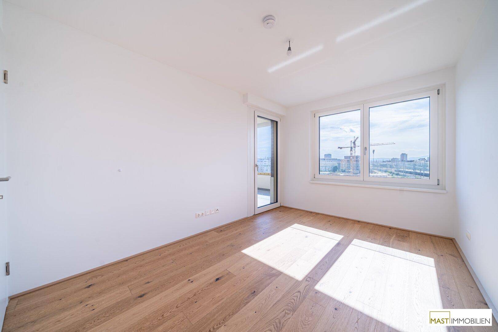 Helles Schlafzimmer mit Holzboden und großen Fenstern, die viel Tageslicht hereinlassen.