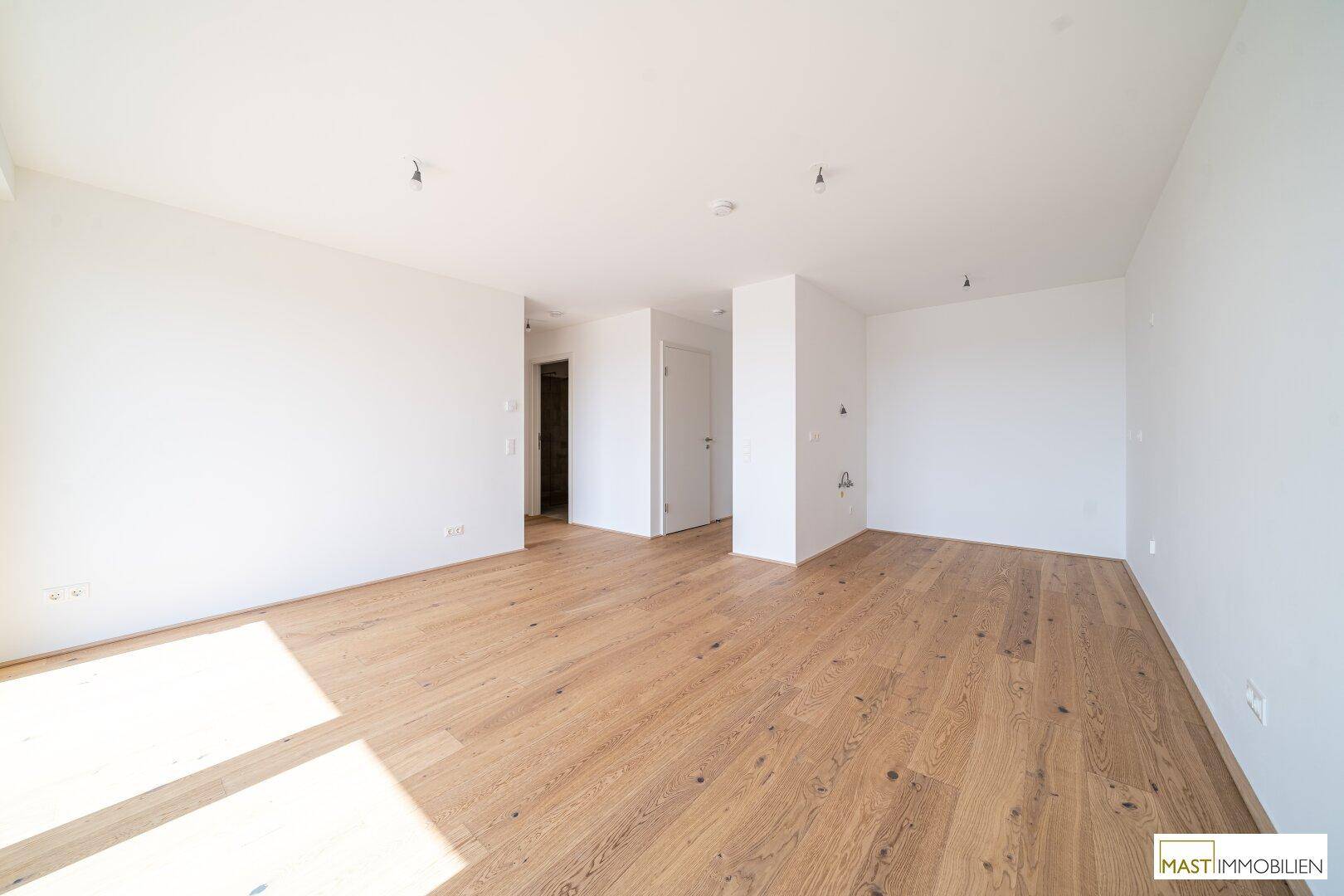 Heller, leerer Raum mit Holzboden und Zugang zu weiteren Zimmern.