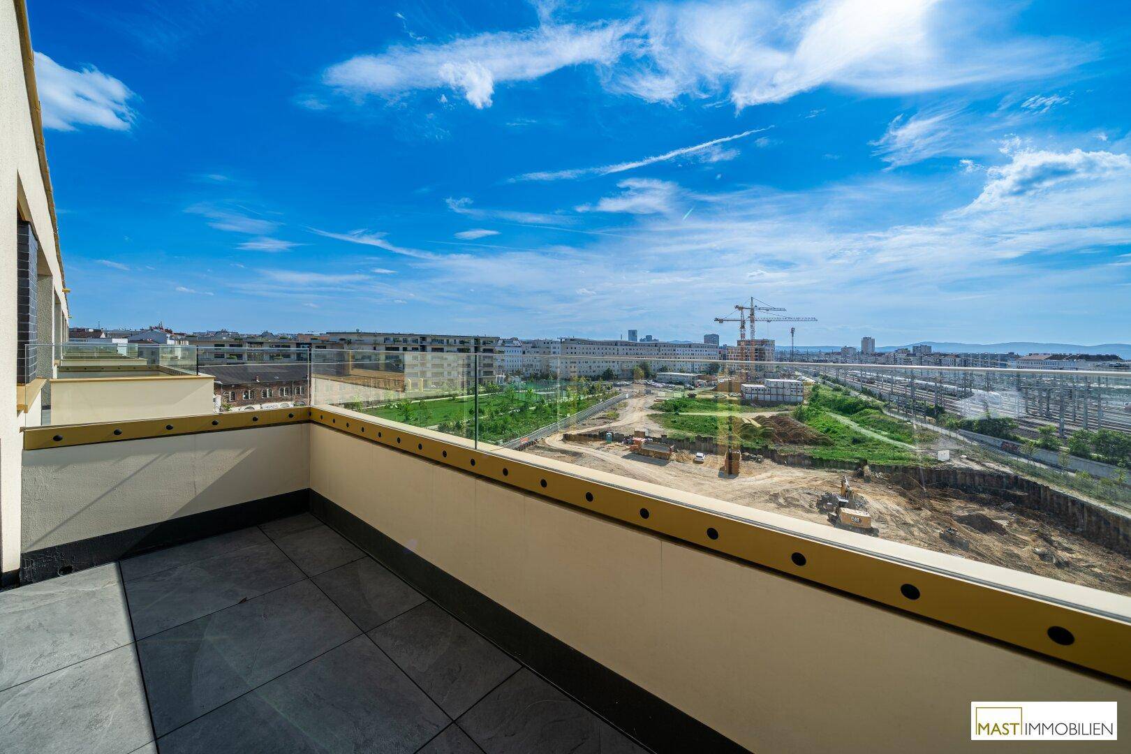 Große Terrasse mit Glasgeländer und weitem Blick auf die Stadt und umliegende Baustellen.