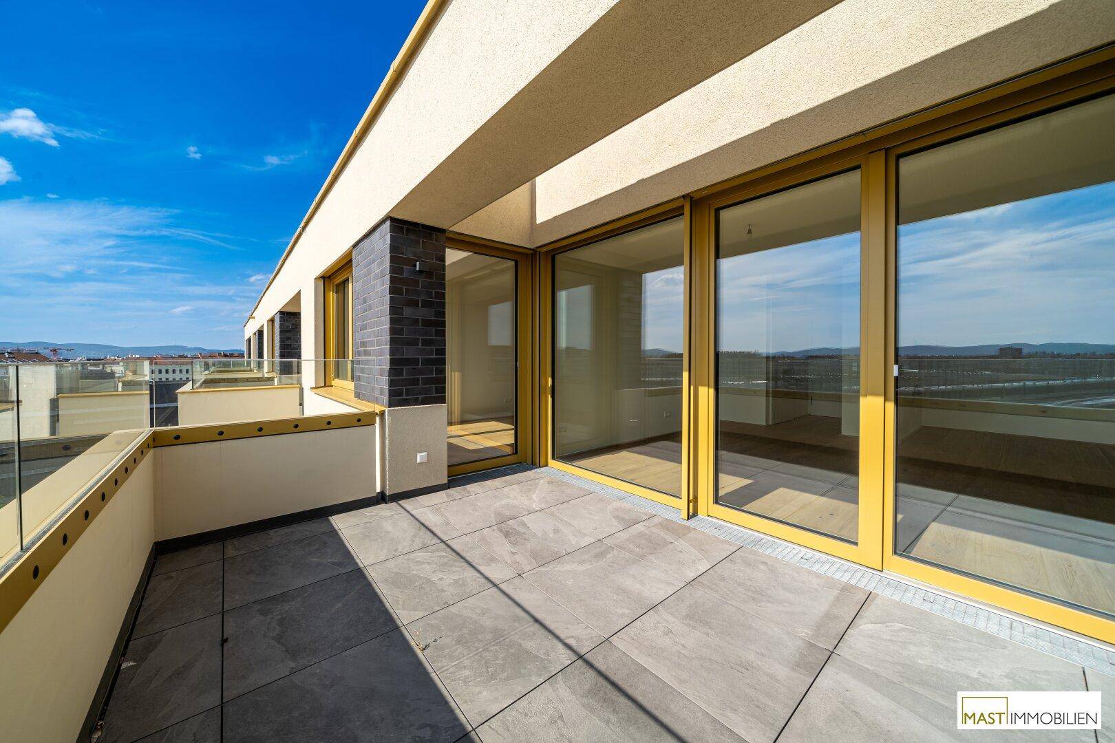 Lange Terrasse mit Fliesenboden und großen Glasfronten, die viel Licht in die Innenräume lassen.