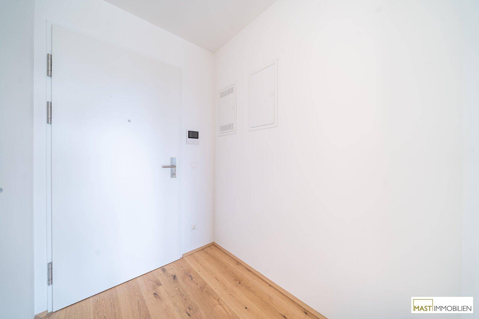Heller Eingangsbereich mit Holzboden und weißer Eingangstür, einladend und funktional gestaltet.