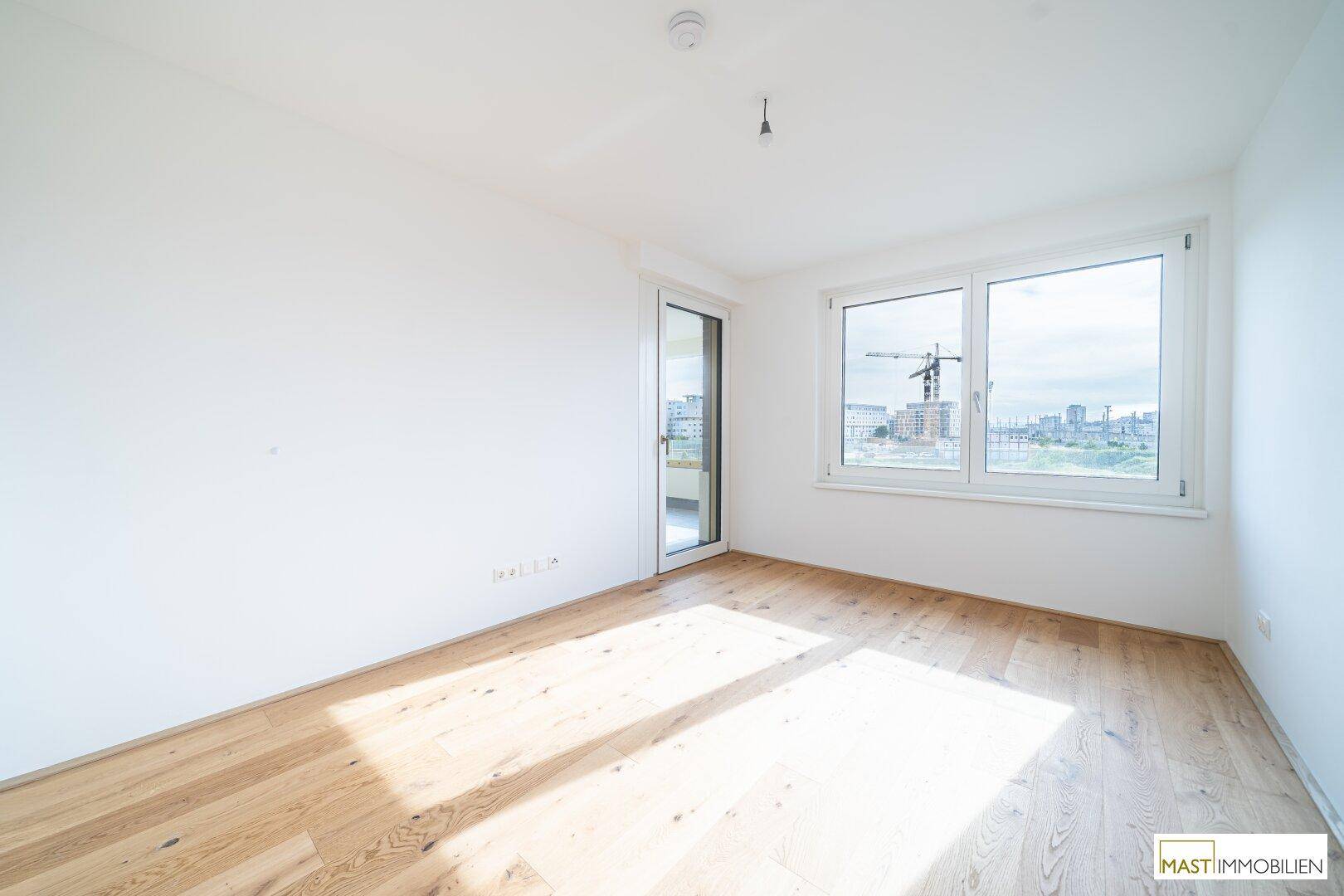 Helles Schlafzimmer mit Holzboden und Zugang zu einem Außenbereich, bietet viel natürliches Licht.