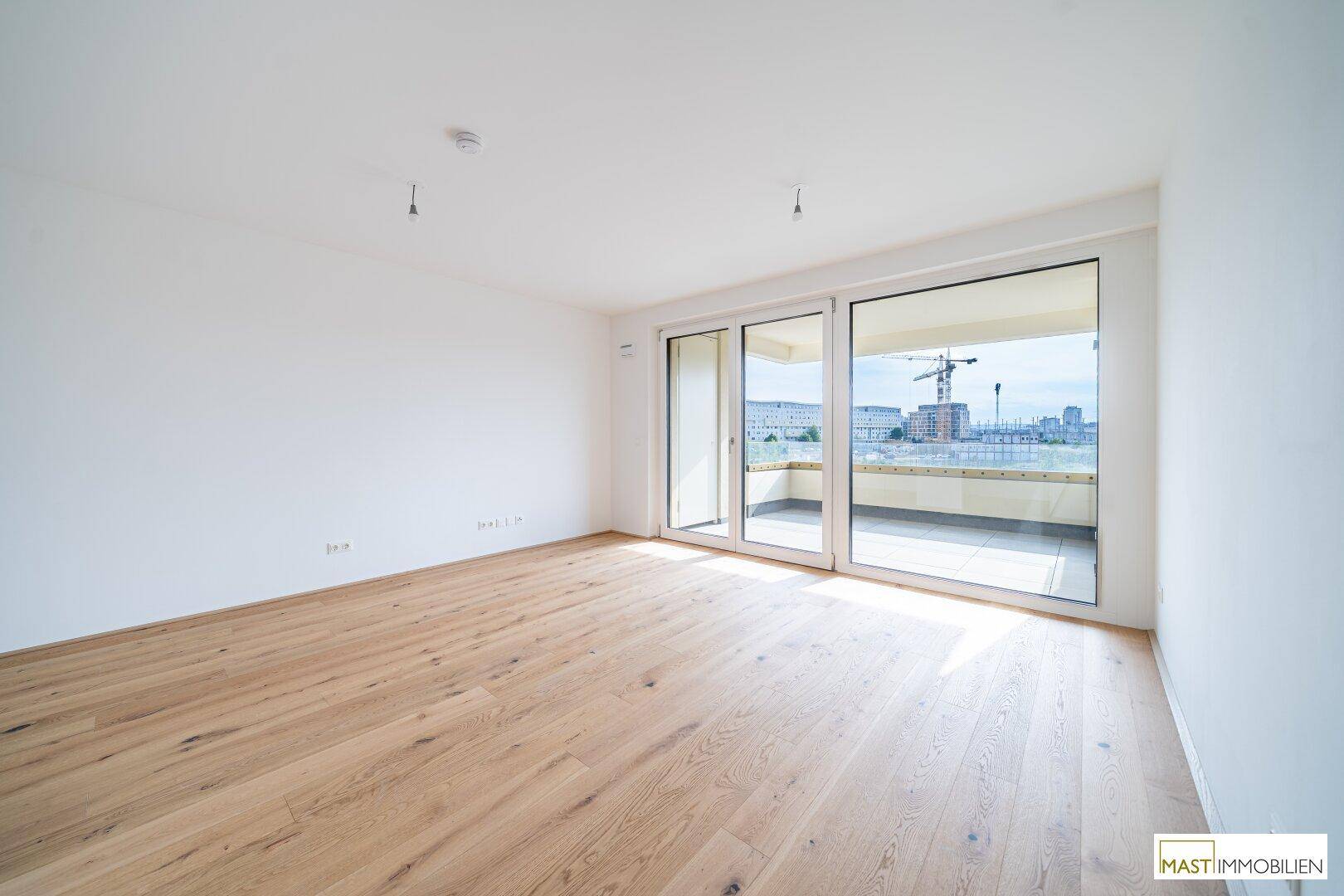 Heller Wohnraum mit Eichenparkett und großen Schiebetüren zum Balkon, bietet viel Tageslicht.