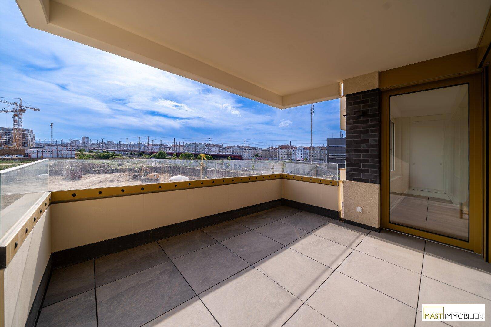 Sonniger Balkon mit Fliesenboden und Glasbrüstung, bietet einen weiten Blick über die Stadtlandschaft.