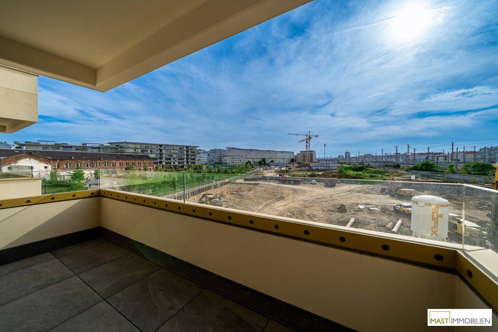 Großer Balkon mit Fliesenboden und Glasgeländer, bietet einen sonnigen Ausblick auf die Stadtentwicklung.
