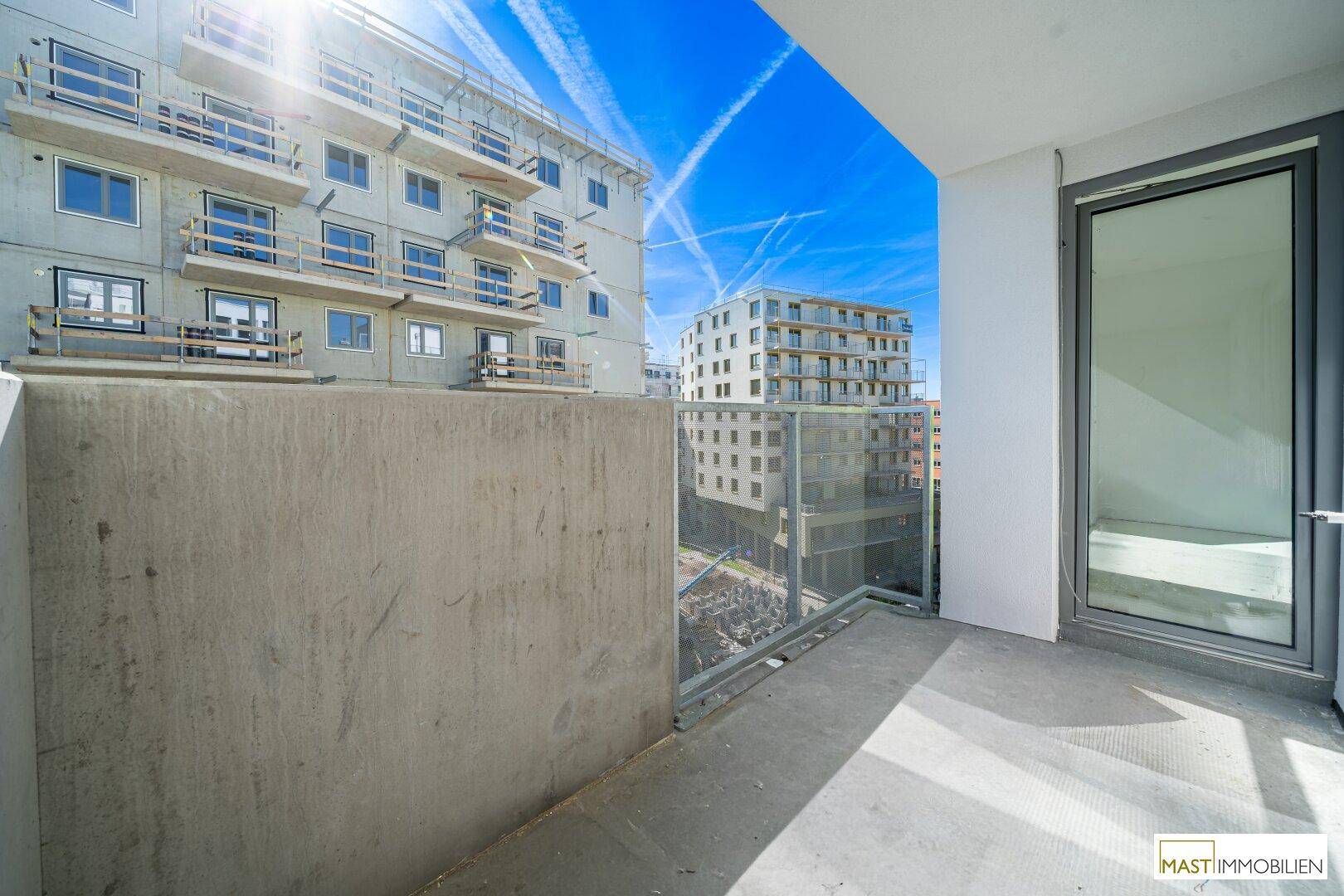 Heller Balkon eines Neubaus mit Glasgeländer und Blick auf weitere moderne Gebäude.