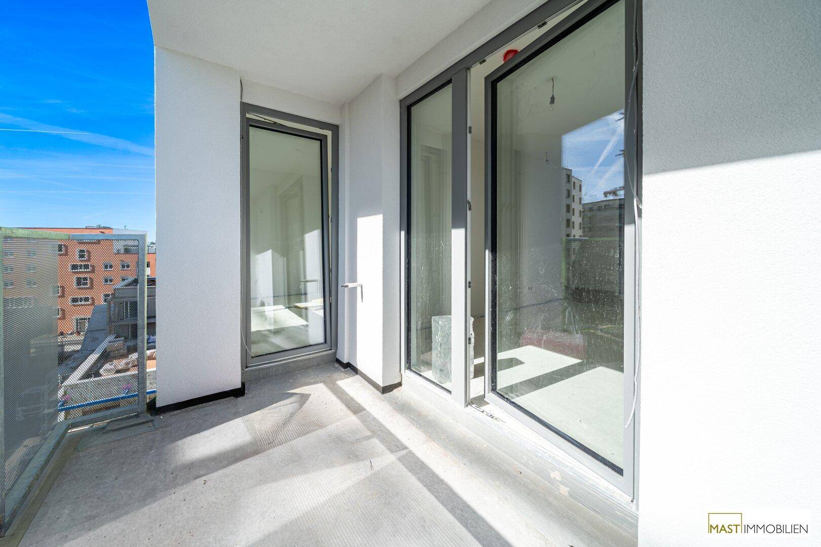 Sonniger Balkon mit großen Schiebetüren, die Zugang zum Innenbereich des Neubaus bieten.