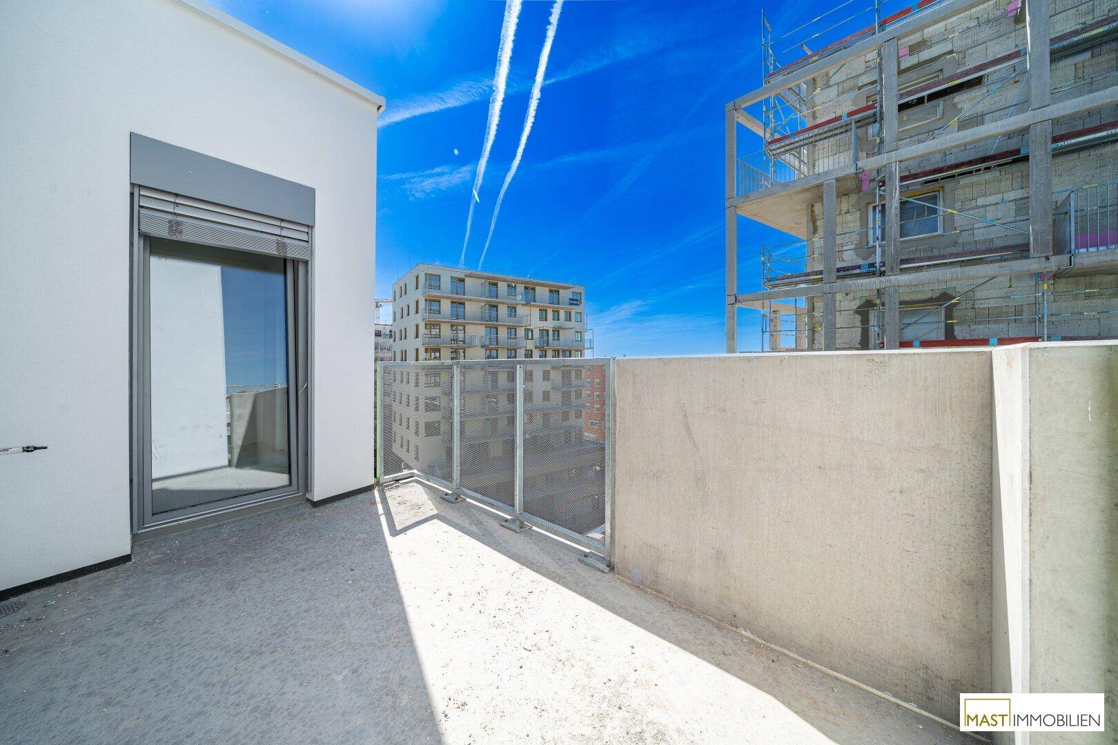 Geräumiger Balkon mit Glasbrüstung und Ausblick auf die umliegende Bebauung und Baustelle.