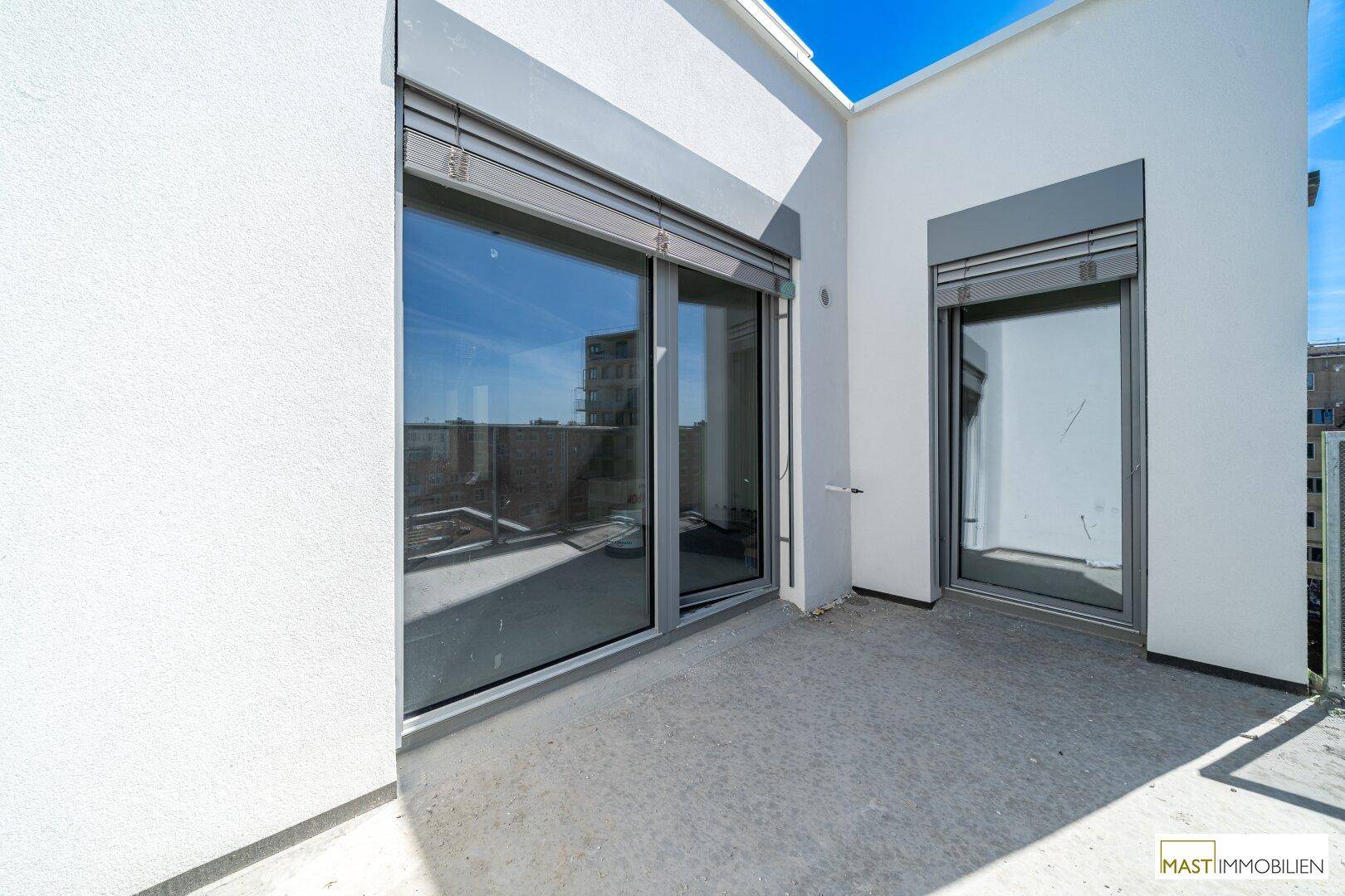 Heller Balkon mit großen Glasfronten, Rollläden und Blick auf die städtische Umgebung.