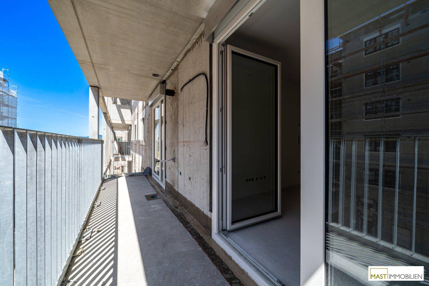 Langer Balkon eines Neubaus mit Zugang zum Innenraum und Blick auf die Baustelle.