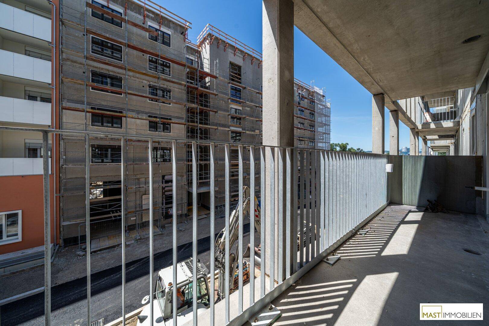Offener Balkonbereich eines Neubaus mit unverputzten Wänden und Blick auf die umliegende Baustelle.