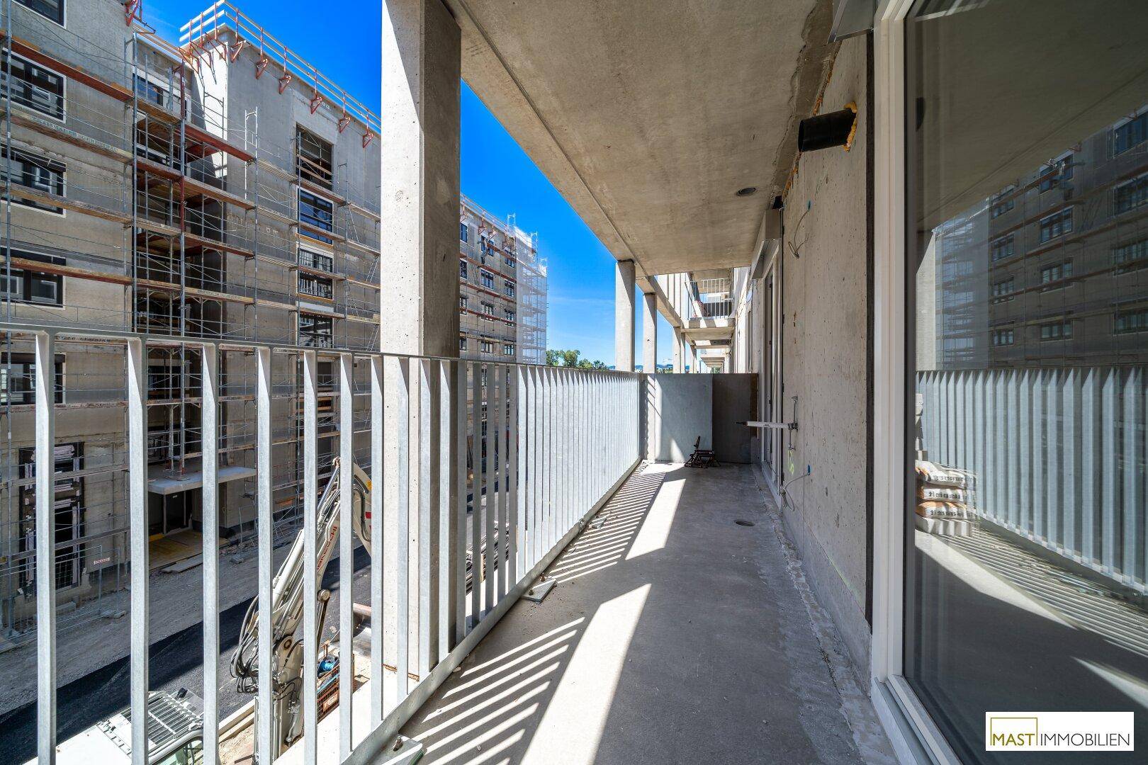 Geräumiger Balkon im Neubau mit Blick auf weitere im Bau befindliche Gebäude und viel Sonnenlicht.