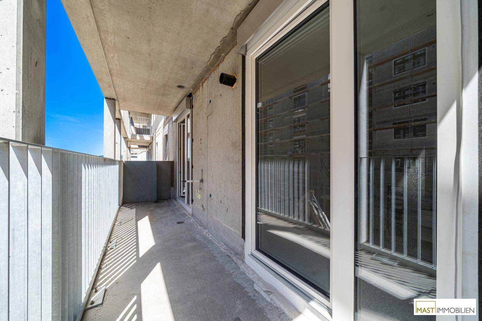 Langer Balkon im Rohbauzustand mit Betonwänden und Metallgeländer, bereit für den Ausbau.