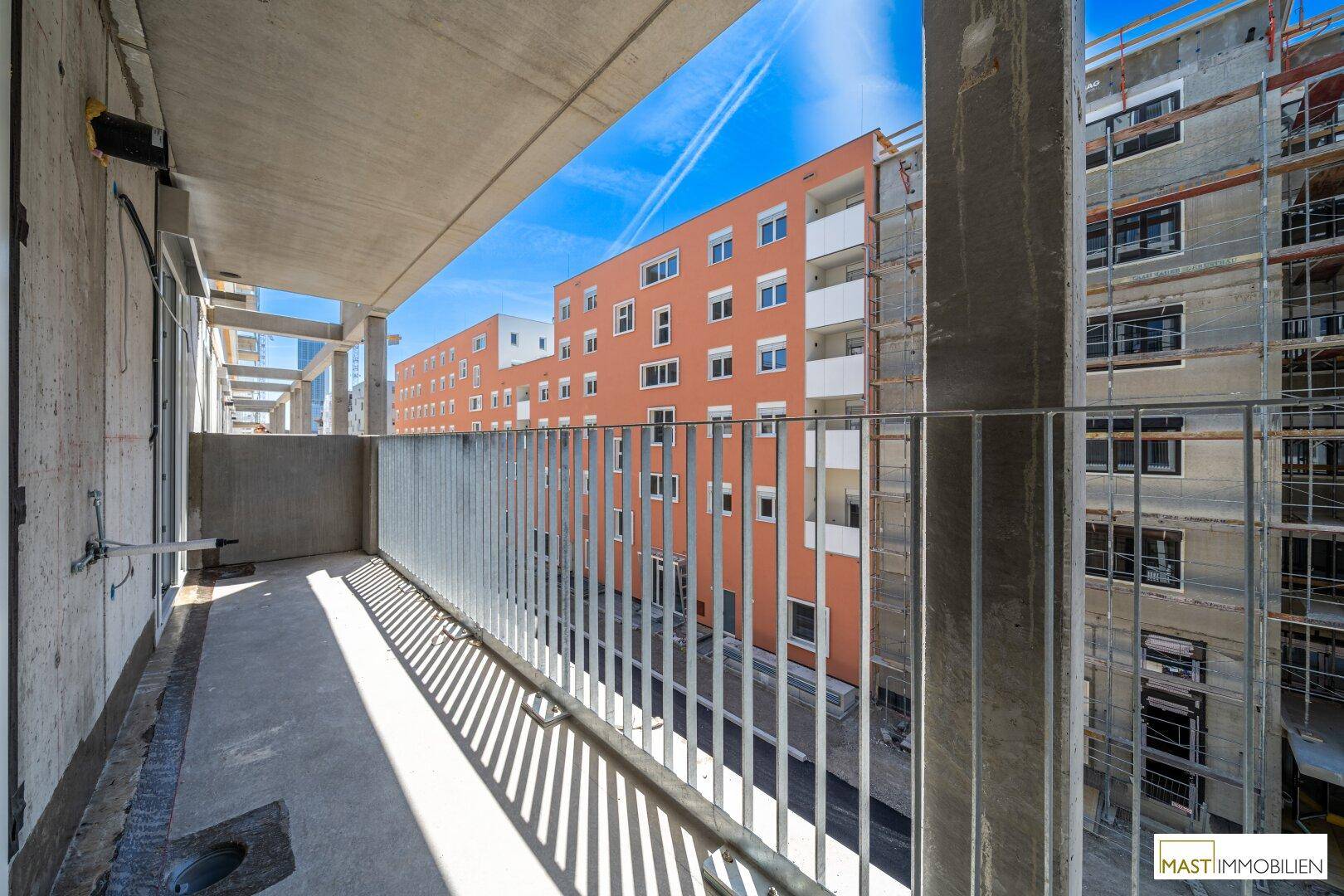 Unfertiger Balkon mit weitem Blick auf umliegende Gebäude, teils im Bau, teils fertiggestellt.