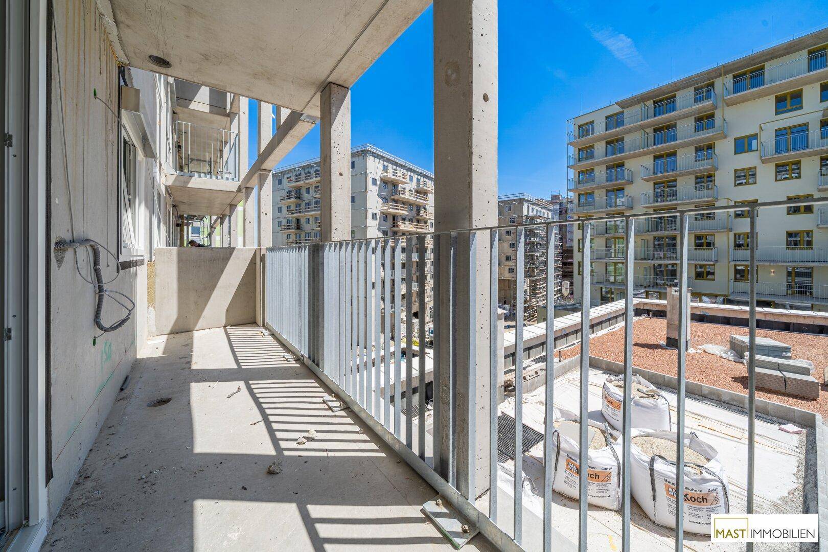 Unfertiger Balkon eines Neubaus mit Blick auf weitere Gebäude im Bau unter blauem Himmel.