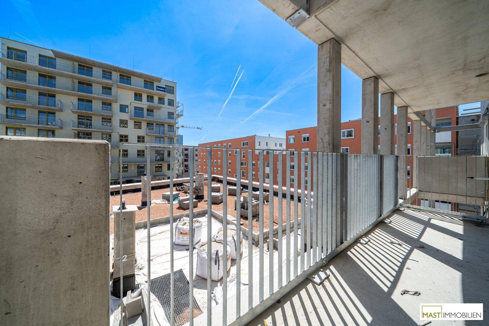 Balkon im Rohbau mit Blick auf die umliegenden Neubauten unter strahlend blauem Himmel.