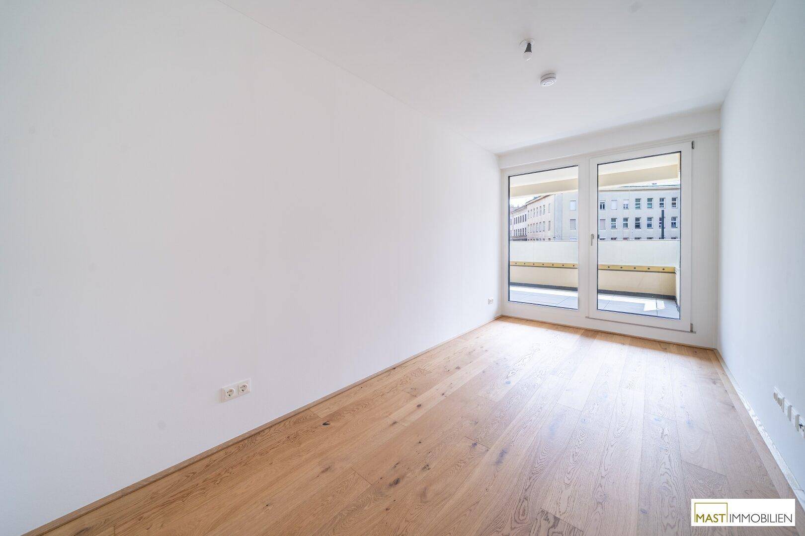 Freundliches Zimmer mit Parkettboden und Zugang zu einem französischen Balkon, der viel Licht spendet.