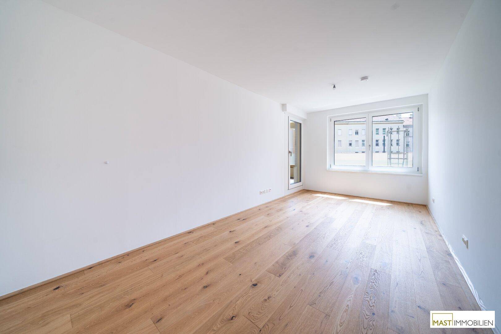 Ruhiges Schlafzimmer mit hellem Parkettboden und großen Fenstern, die viel Tageslicht hereinlassen.