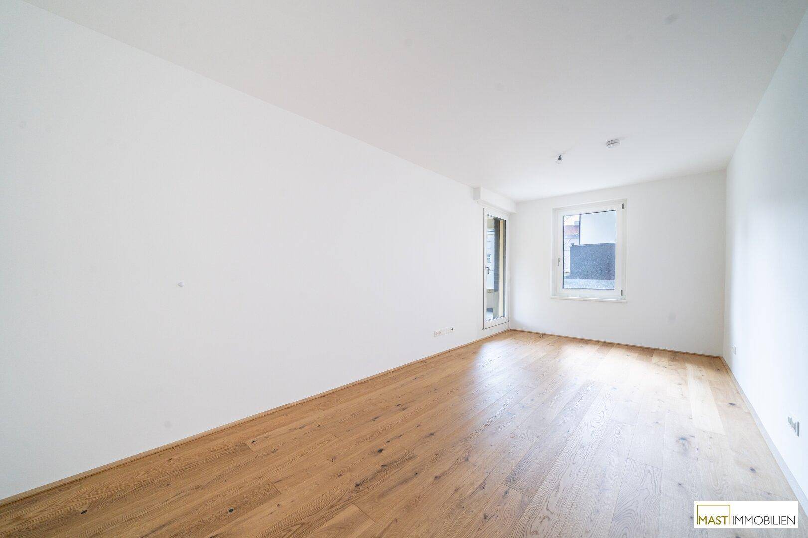 Heller Raum mit Holzboden, einem Fenster und Balkonzugang, der eine flexible Nutzung erlaubt.