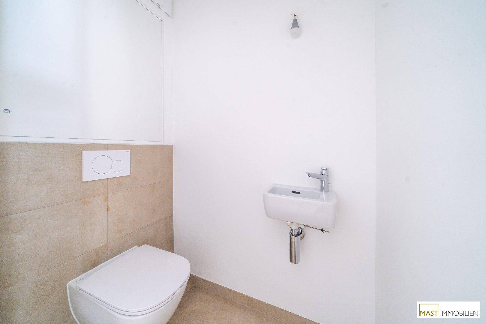 Separates WC mit wandhängender Toilette und kleinem Handwaschbecken, modern gefliest.