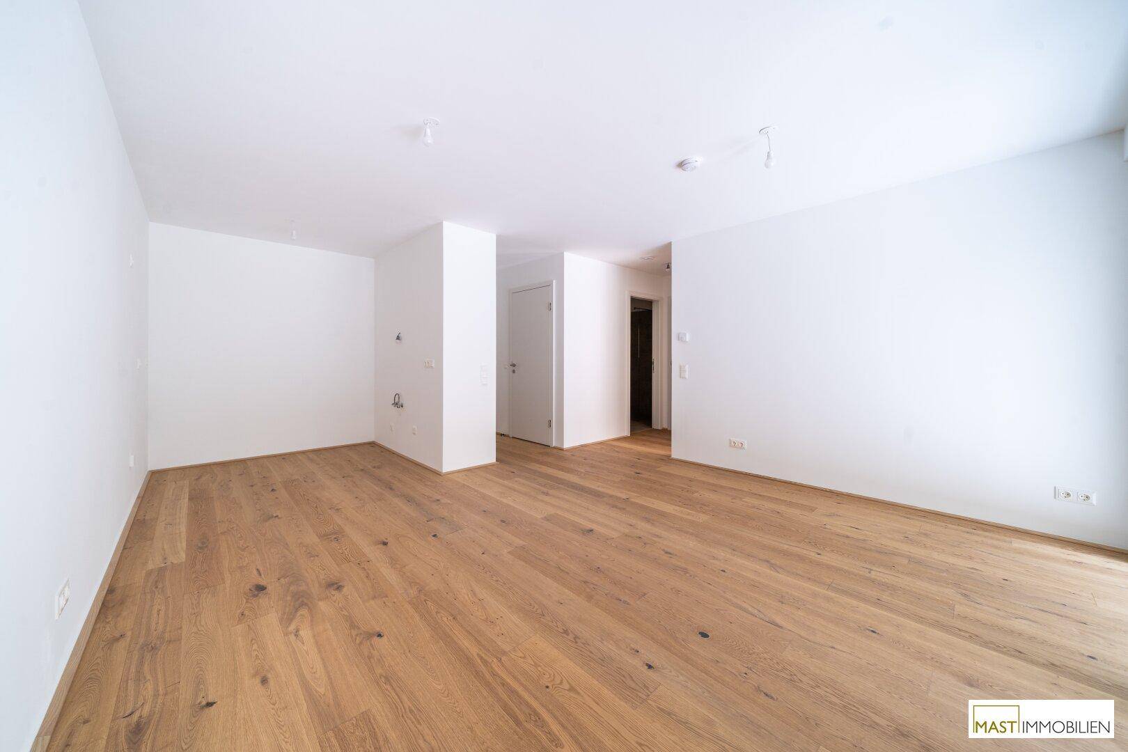 Geräumiger, leerer Raum mit hellem Holzboden und weißen Wänden, vielseitig nutzbar.