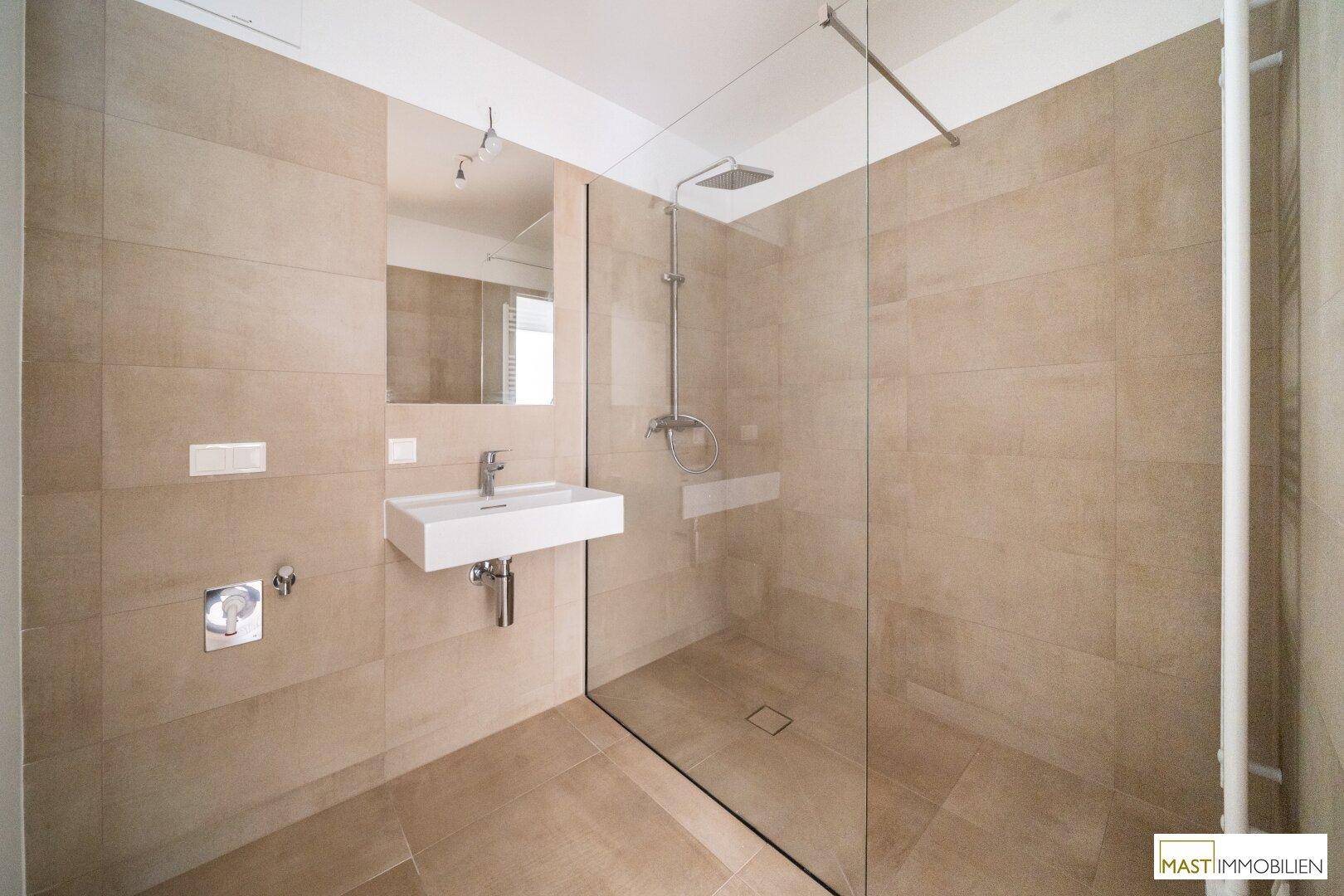 Helles Badezimmer mit großer begehbarer Dusche, modernem Waschbecken und beigefarbenen Fliesen.