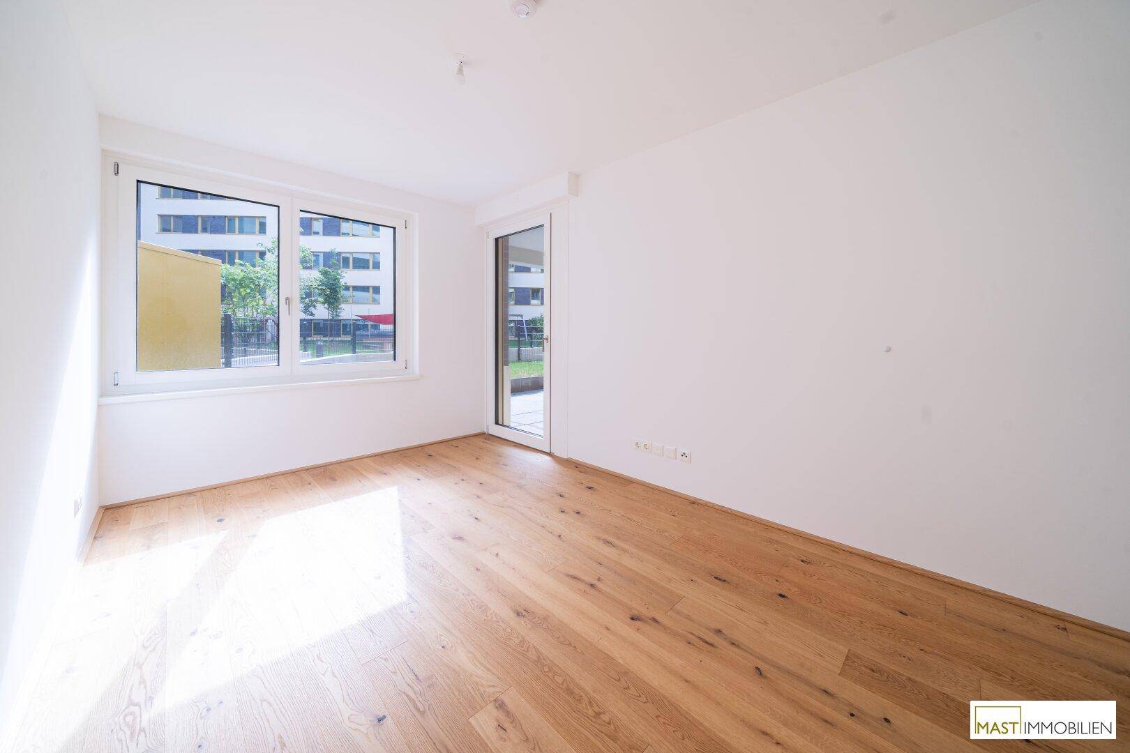 Schlafzimmer mit Holzboden, großem Fenster und Zugang zum Außenbereich, hell und freundlich.