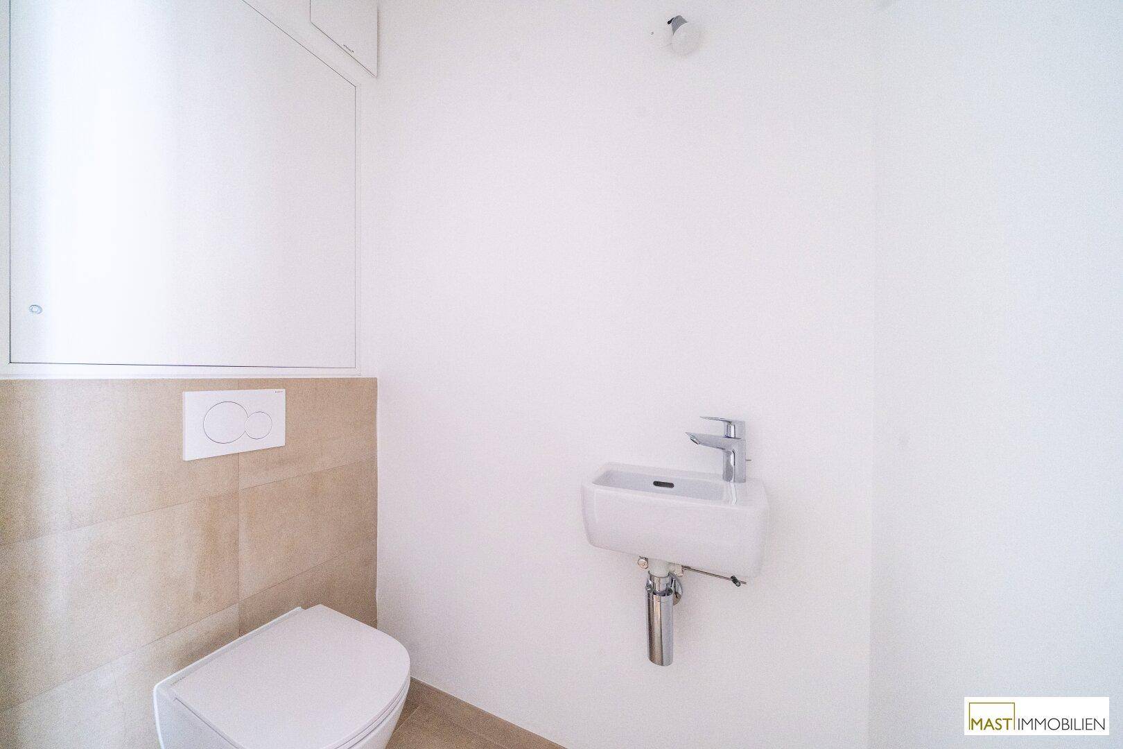 Modernes Gäste-WC mit wandhängendem WC, kleinem Waschbecken und beigen Fliesen.