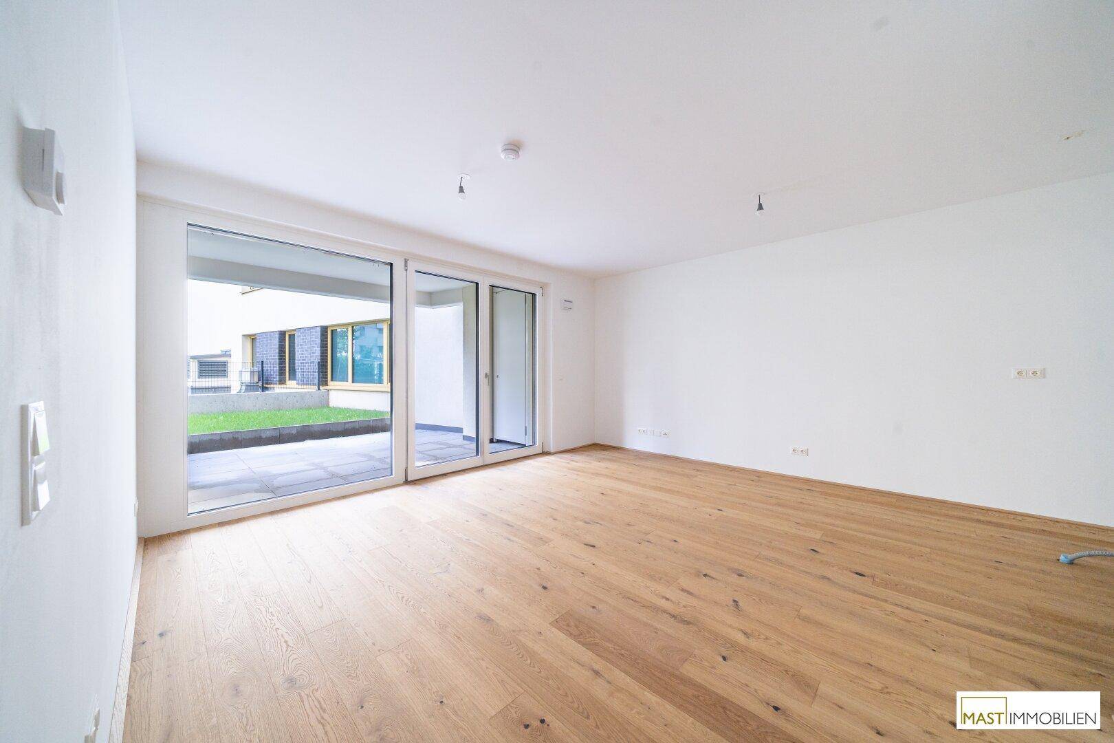 Heller, leerer Wohnraum mit Eichenparkettboden und großen Schiebetüren zur Terrasse.