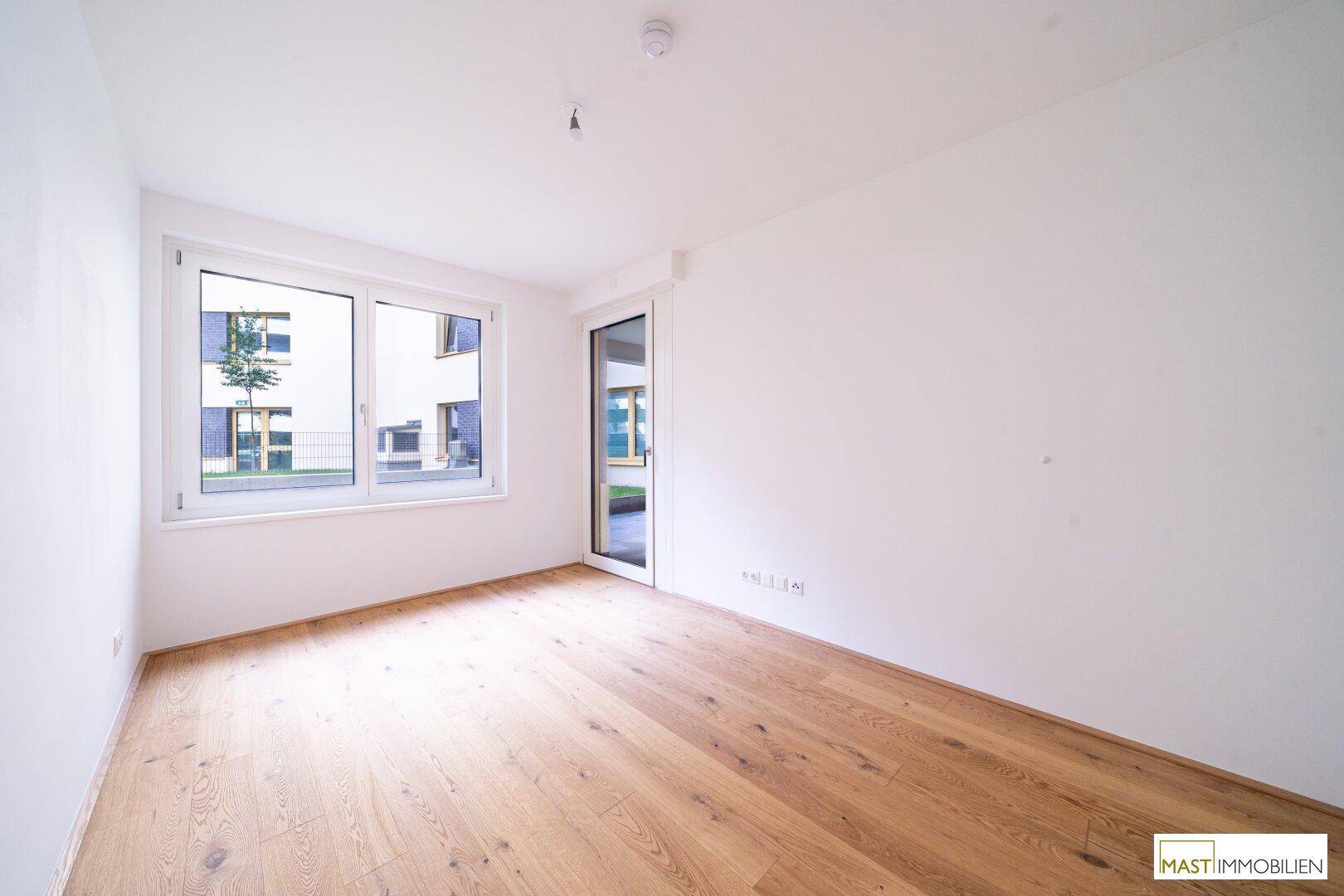 Helles Schlafzimmer mit Parkettboden und Fenster sowie Tür zum Außenbereich.