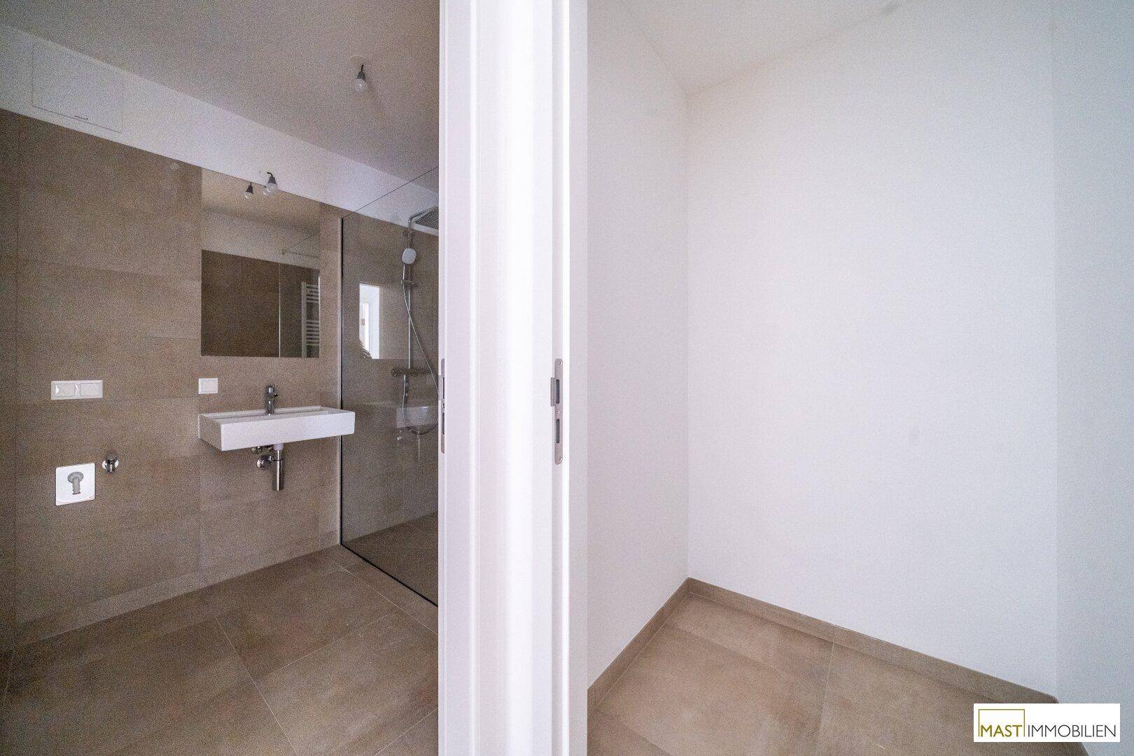 Blick in ein modernes Badezimmer mit begehbarer Dusche und beigen Wandfliesen.