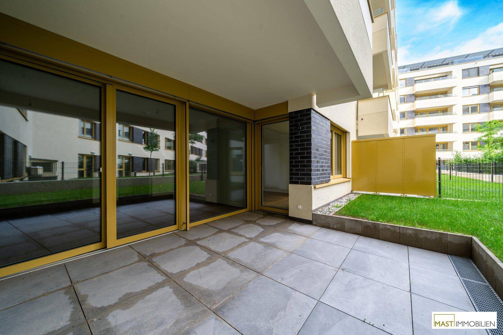 Großzügige, geflieste Terrasse mit Schiebetüren und angrenzendem Grünbereich.