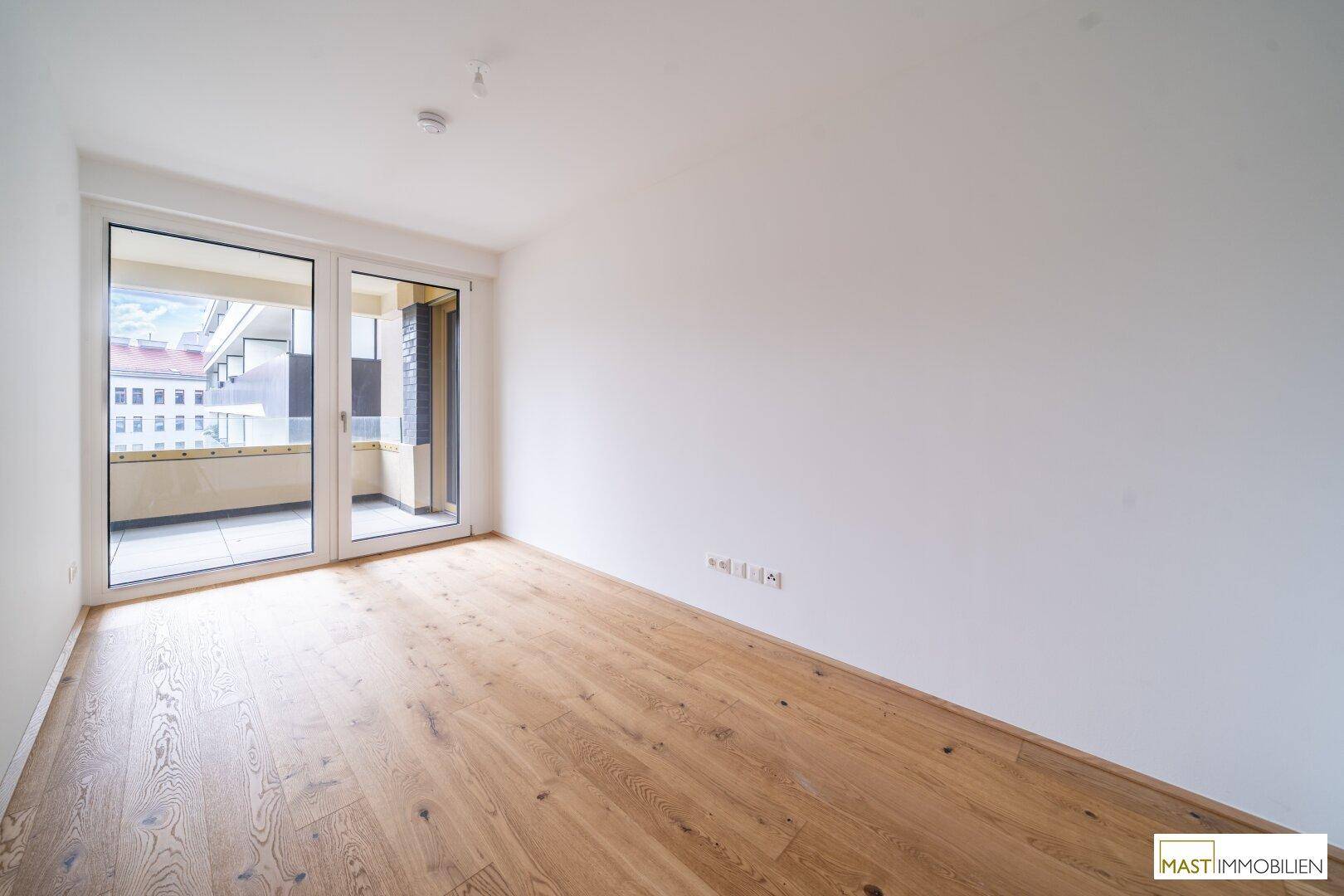 Helles Schlafzimmer mit Holzparkett und Zugang zu einem Balkon, bietet viel Tageslicht.