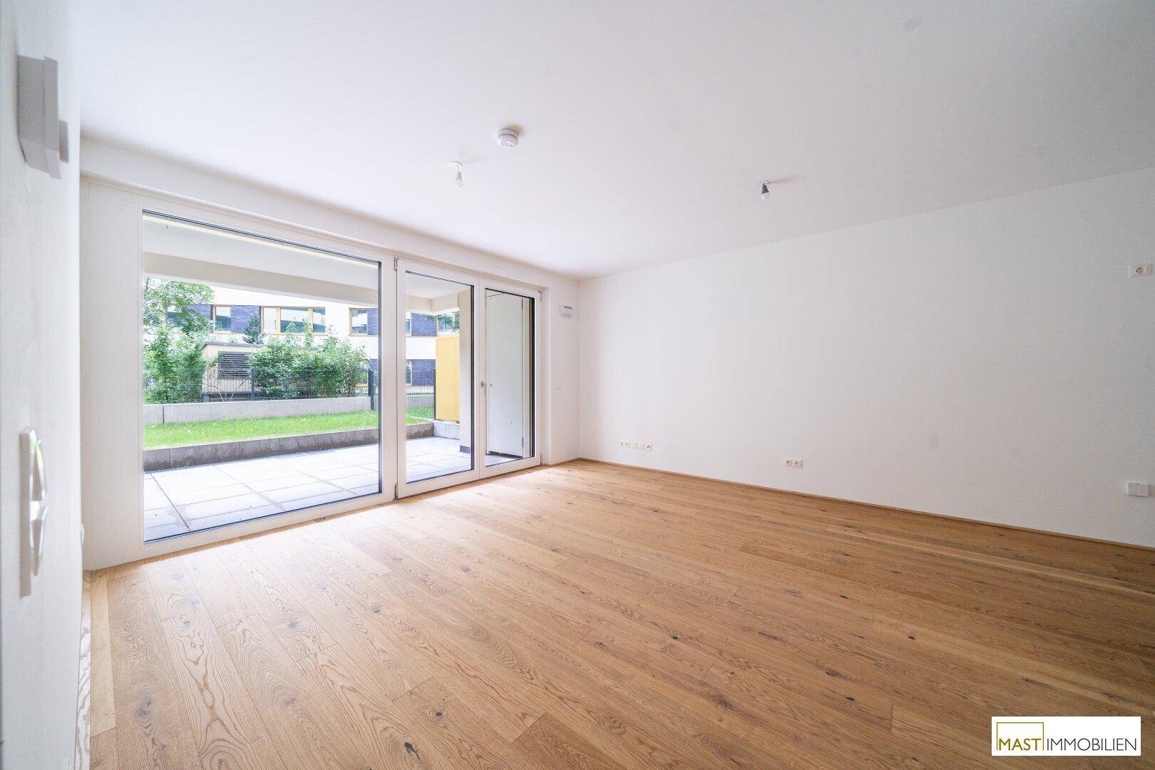 Heller Wohnraum mit großen Fenstern, Holzboden und direktem Zugang zur Terrasse.