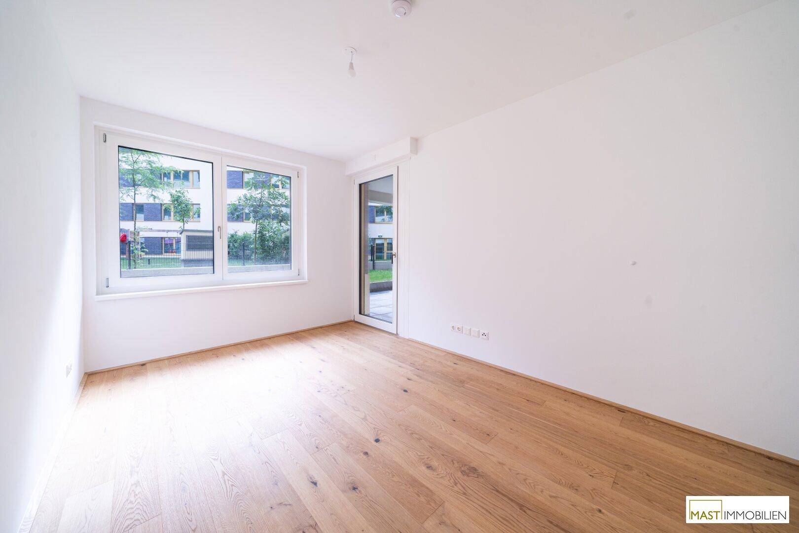 Helles Zimmer mit Holzboden und großen Fenstern, ideal als Schlafzimmer oder Büro.