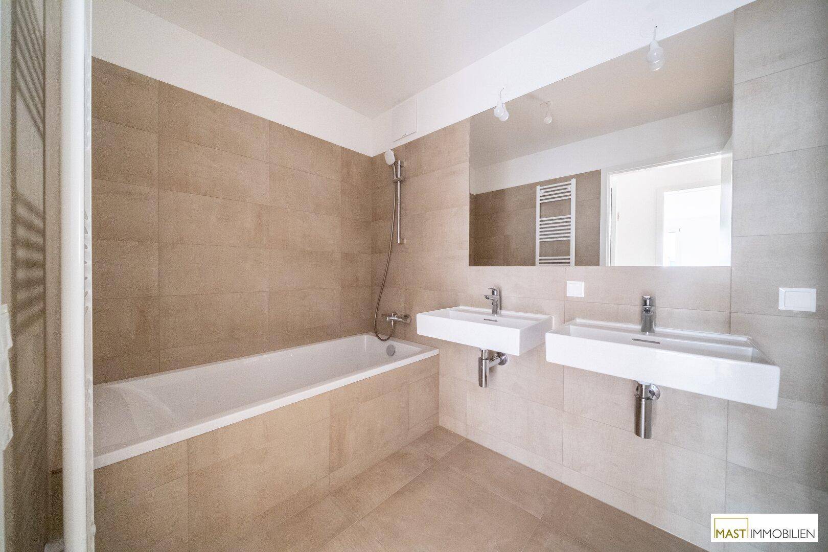 Modernes Badezimmer mit doppelten Waschbecken, Badewanne und beigefarbenen Fliesen.