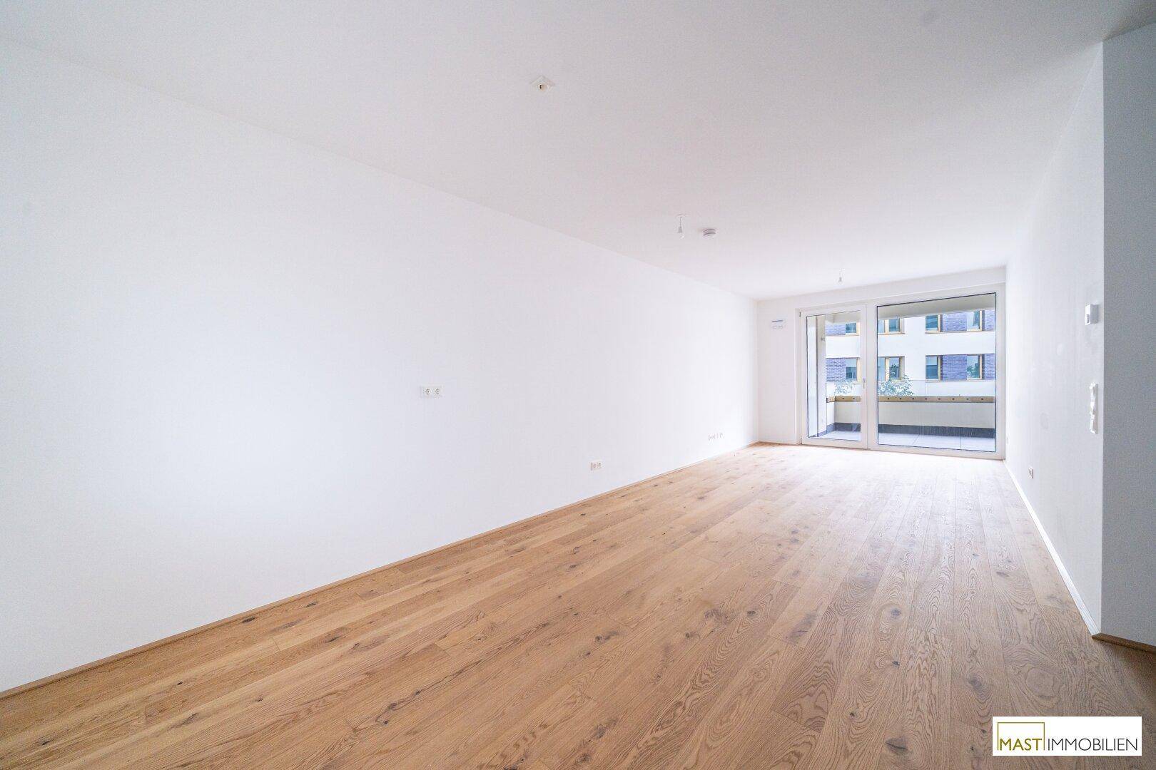 Geräumiges Zimmer mit hellem Parkettboden und Zugang zu einem Balkon, ideal für Wohnbereich.