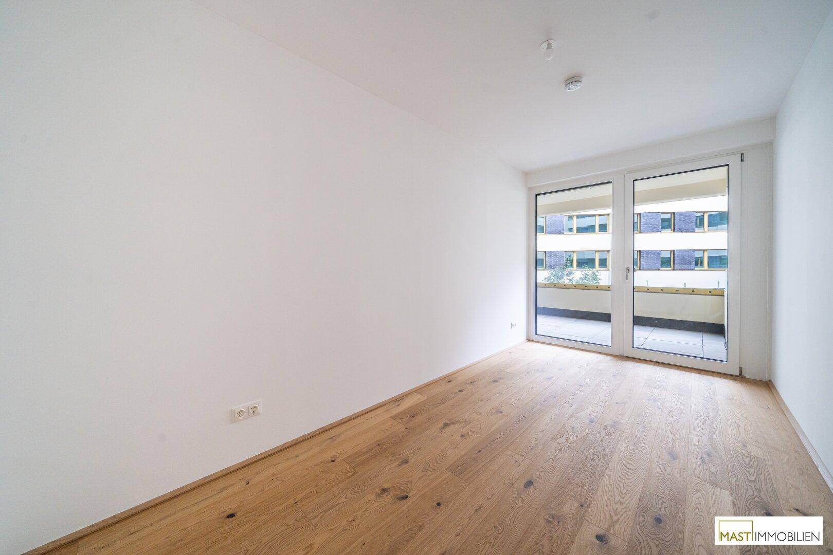 Helles Schlafzimmer mit Parkettboden und direktem Zugang zum Balkon, mit Blick auf den Innenhof.