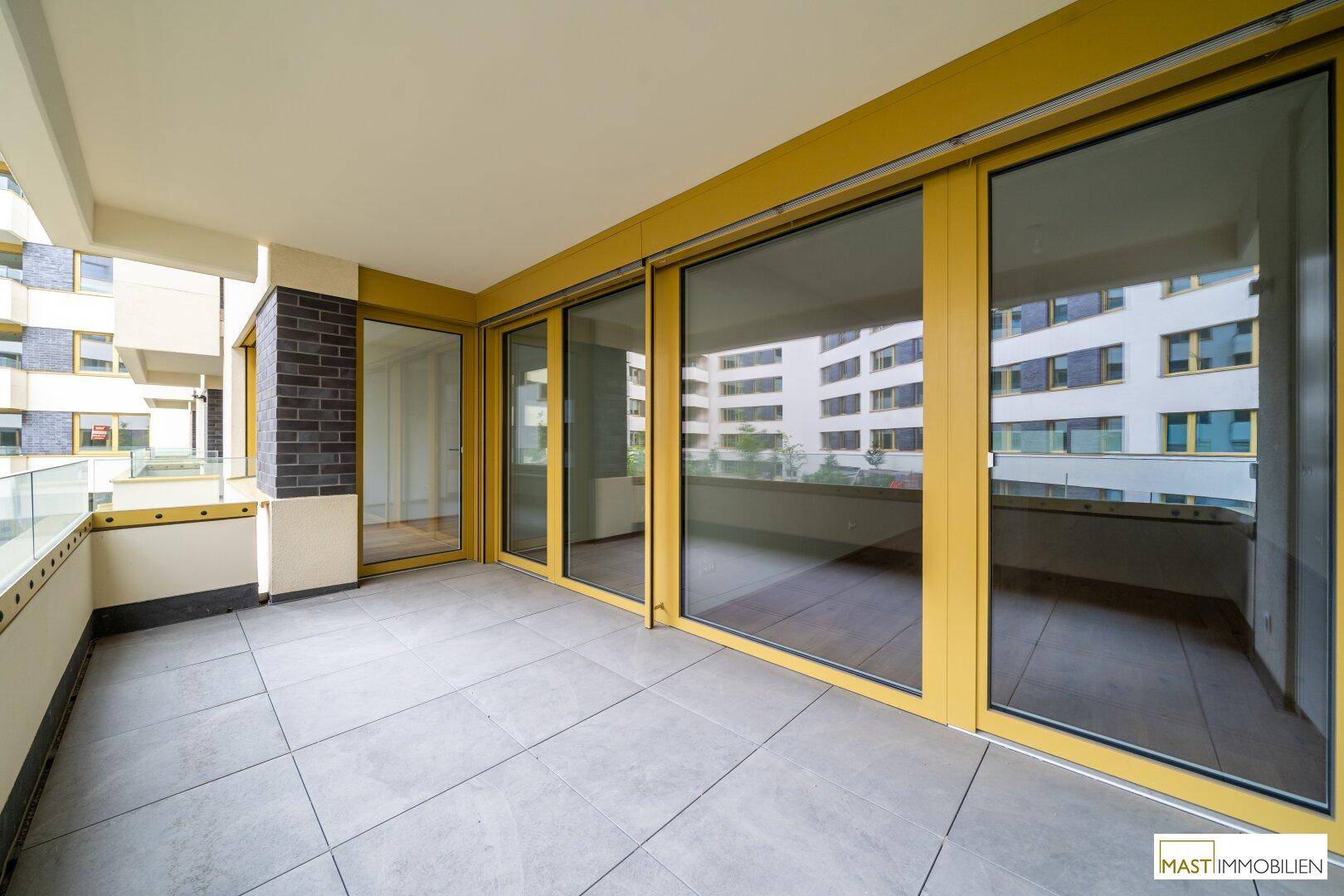 Großer Balkon mit Fliesenboden und raumhohen Glasschiebetüren, bietet viel Licht.