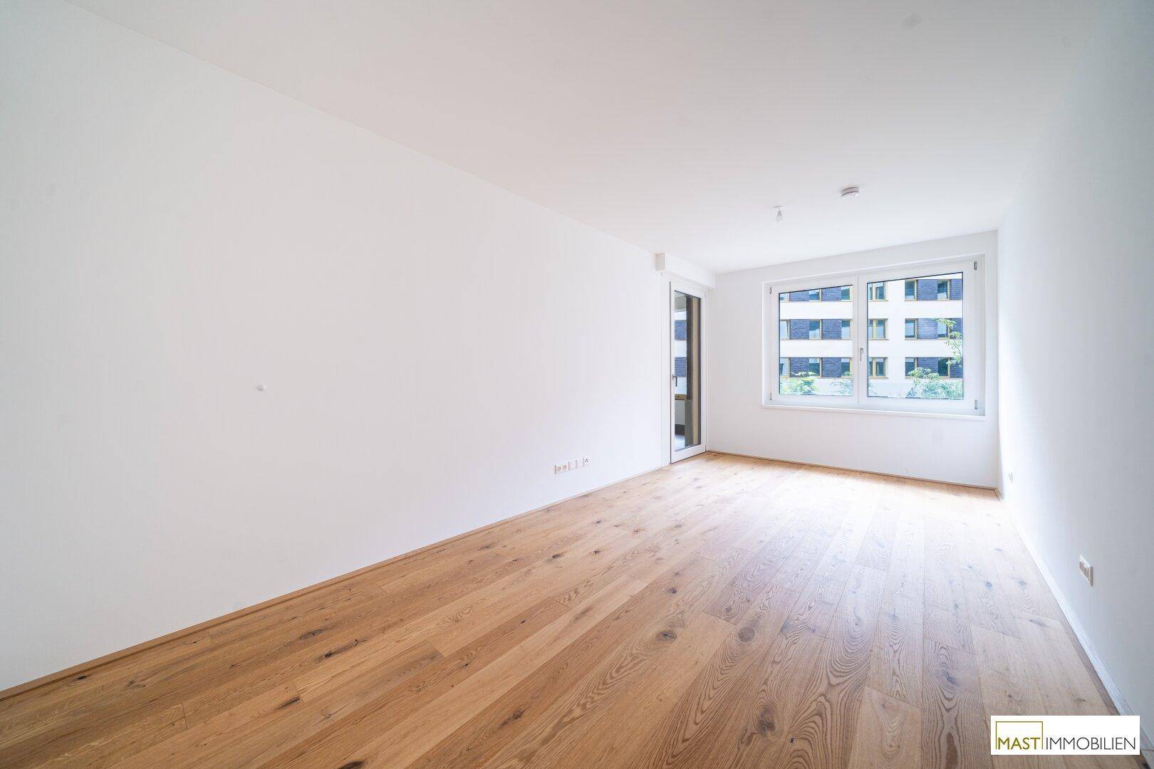 Helles Schlafzimmer mit Parkettboden und großem Fenster, das viel natürliches Licht in den Raum bringt.