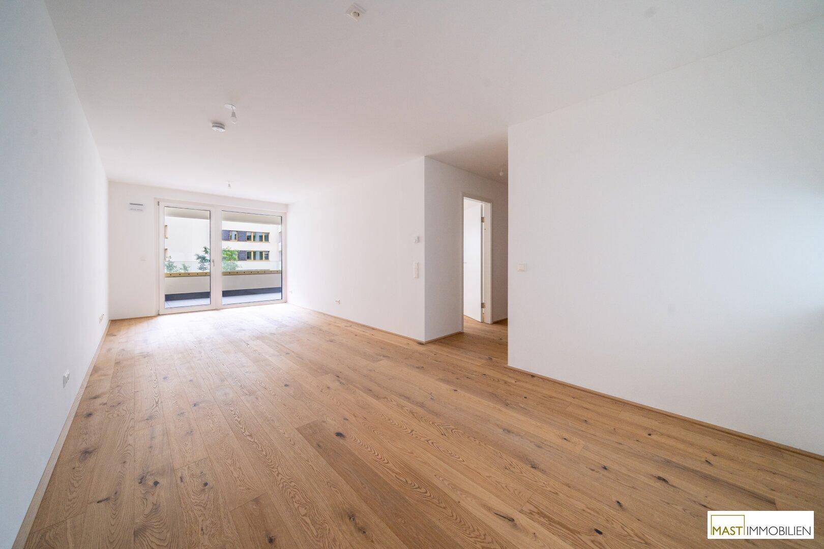 Heller Wohnbereich mit Holzboden und direktem Zugang zum Balkon, offen gestaltet.
