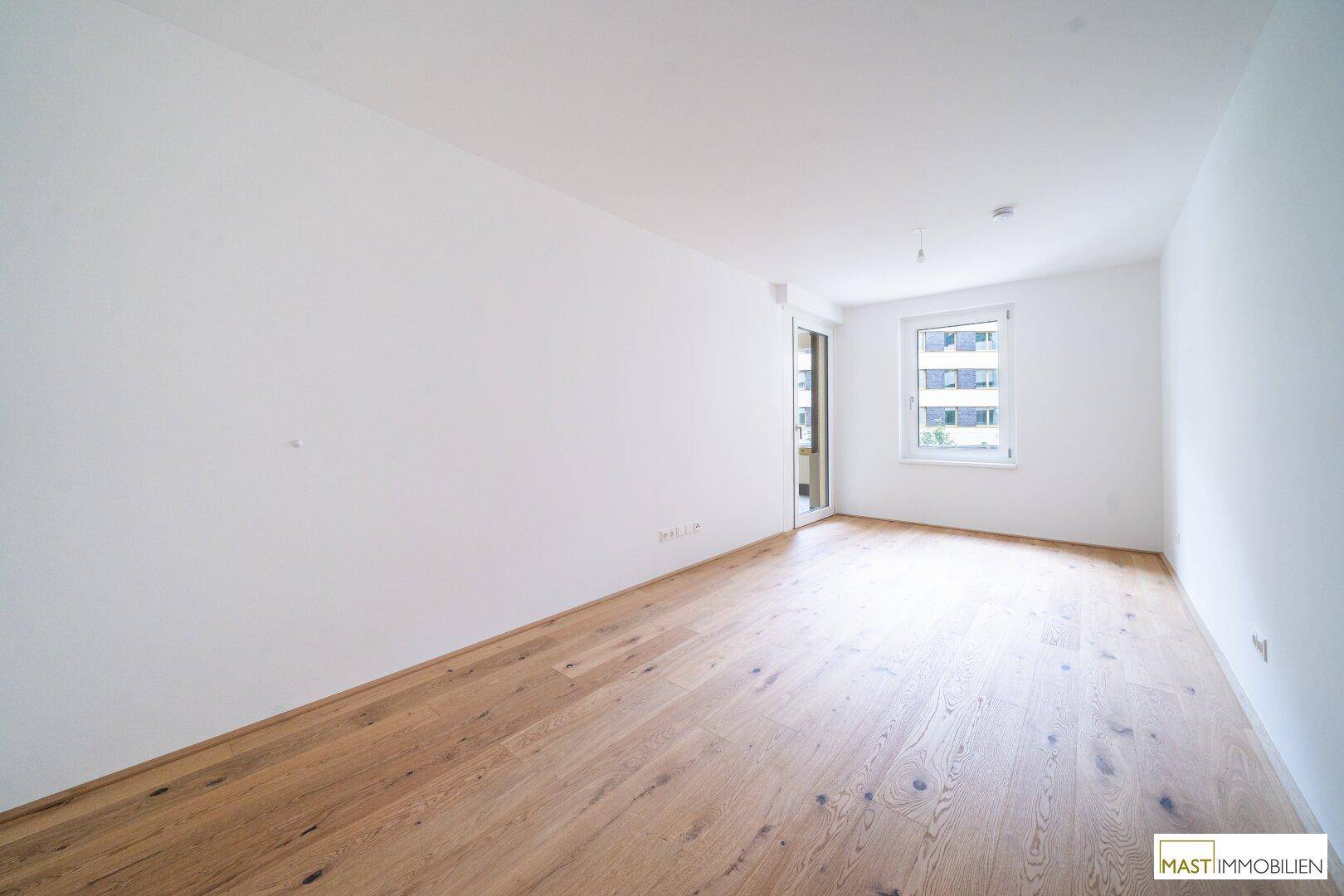 Lichtdurchflutetes Schlafzimmer mit Holzboden und Fenster mit Blick ins Grüne.