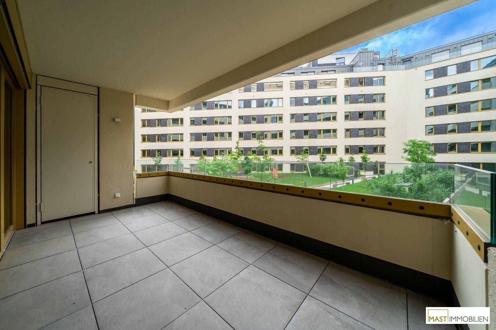 Geräumiger Balkon mit Fliesenboden und Glasgeländer, bietet Blick auf den Innenhof.