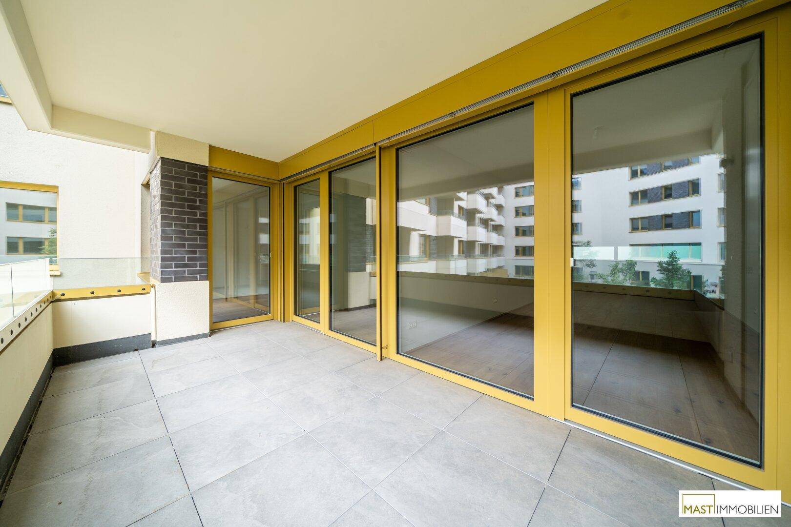 Heller Balkon mit großen Schiebetüren und gelben Rahmen, bietet viel Tageslicht.