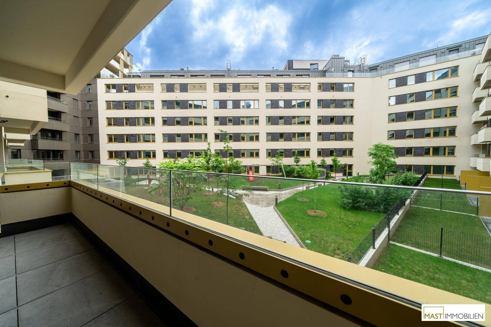 Balkon mit Blick auf den begrünten Innenhof und die moderne Wohnanlage.