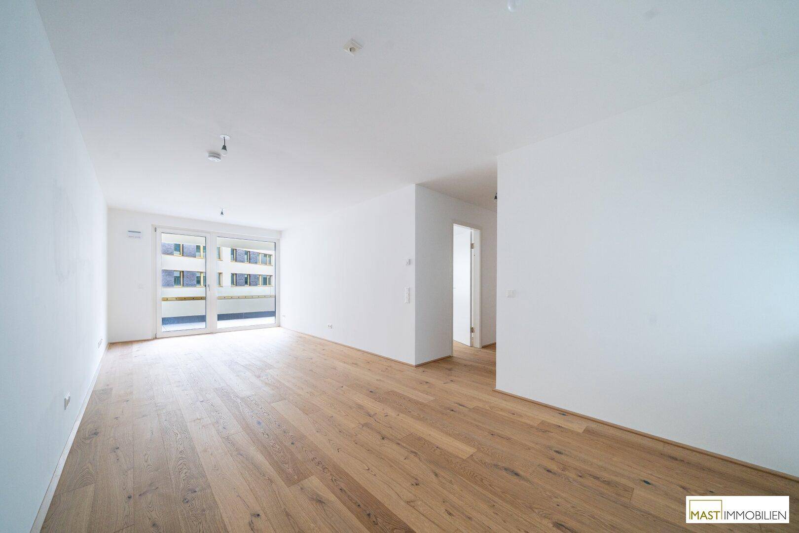 Heller, leerer Wohnbereich mit neuem Holzparkettboden und großen Schiebetüren zum Balkon.