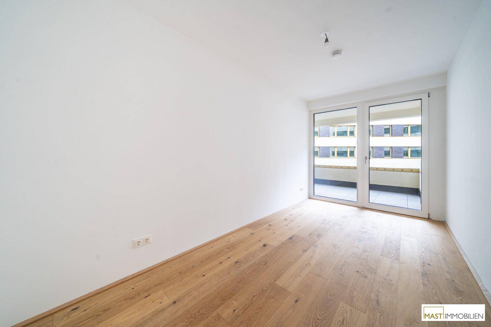 Weiteres helles Schlafzimmer mit Holzparkettboden und großen Fenstern, die viel Tageslicht hereinlassen.