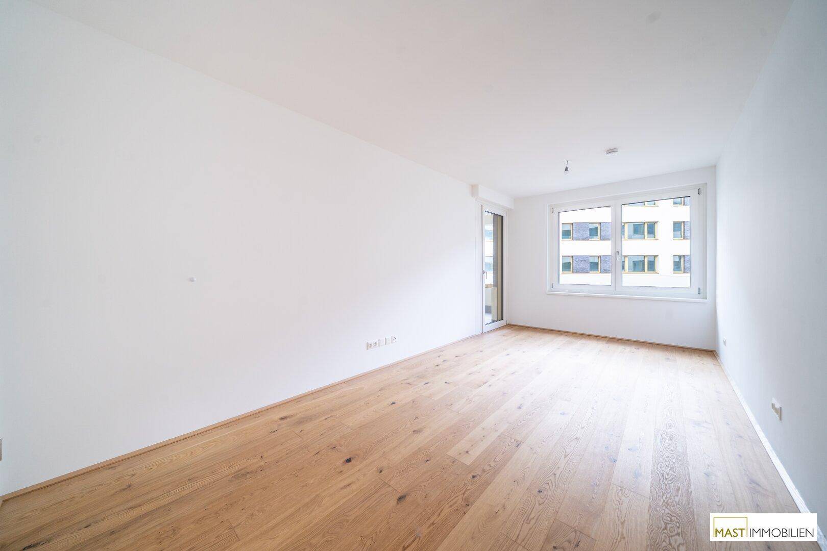 Leeres Zimmer mit Holzparkettboden und großen Fenstern, die einen hellen und freundlichen Raum schaffen.