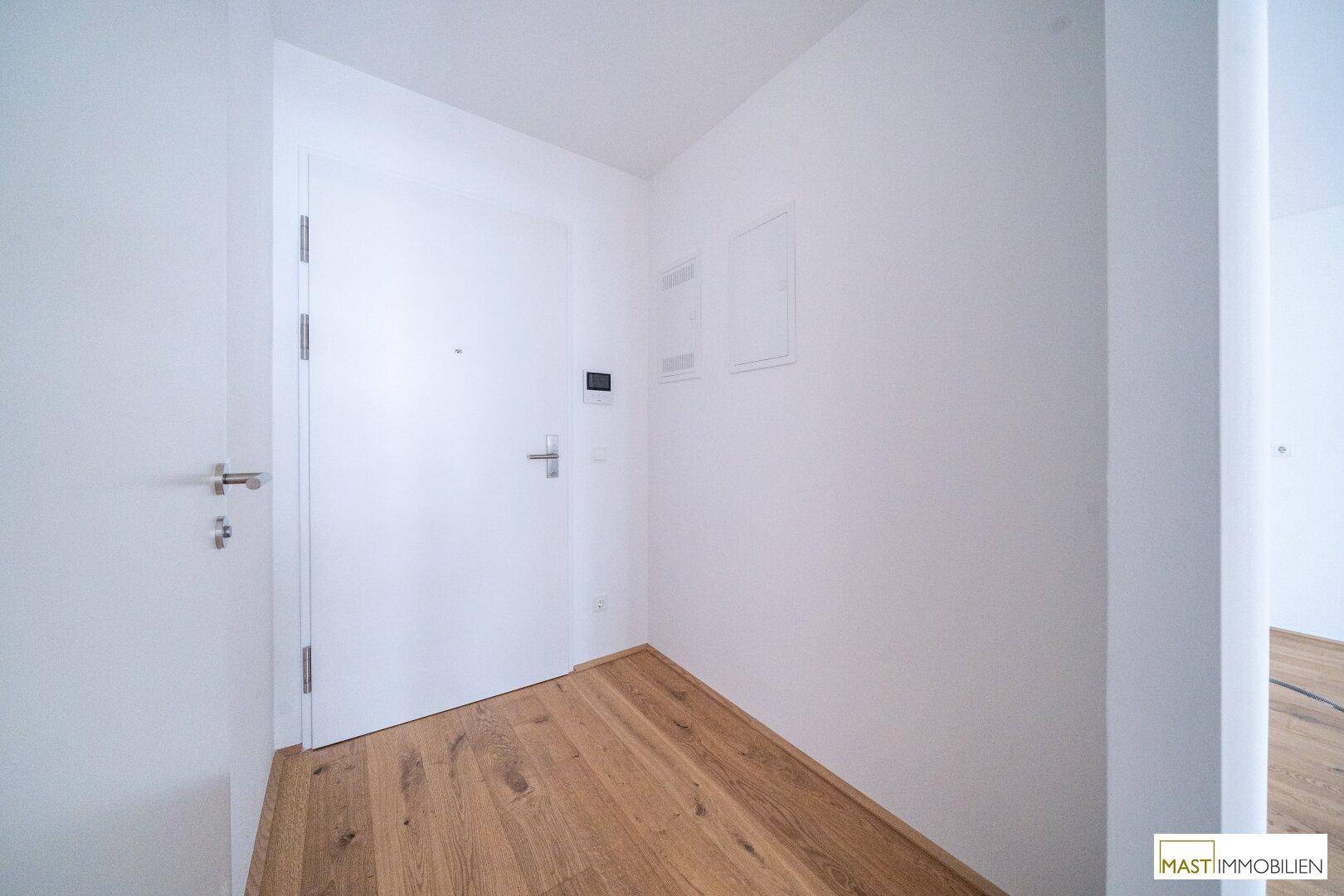 Heller Eingangsbereich mit Holzboden und moderner weißer Tür, einladend und funktional gestaltet.